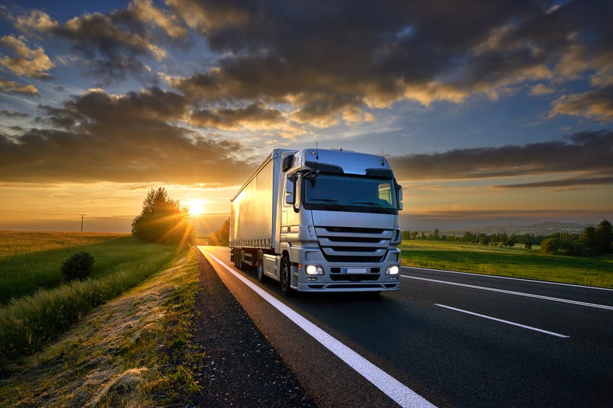 Truck driving on the asphalt road in rural landscape at sunset with dark clouds